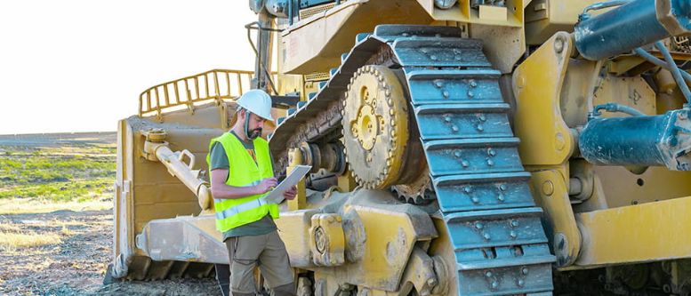 Inspector looking at the tracks and undercarriage of a large used earthmoving bulldozer